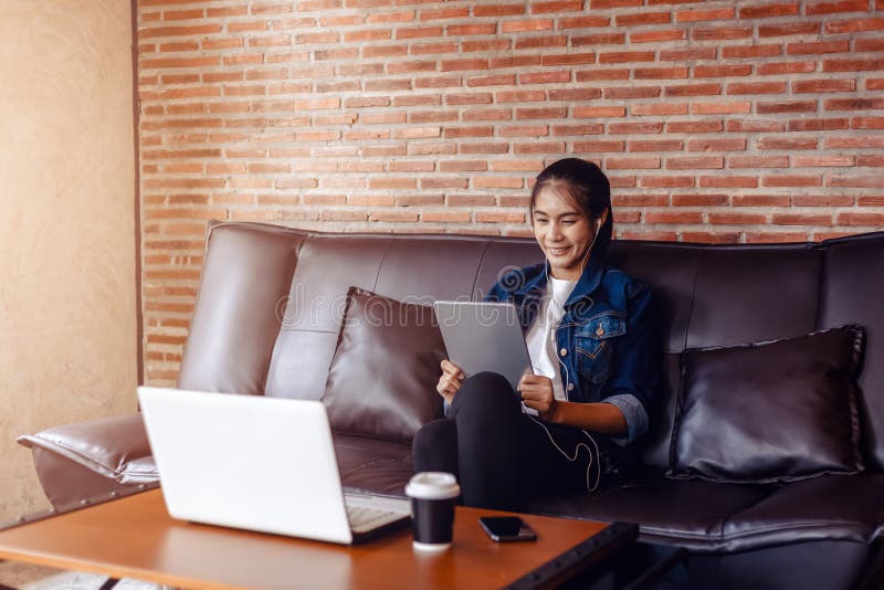 Young happy woman sitting on sofa and using a tablet, laptop on the table in front of her. relaxing concept.