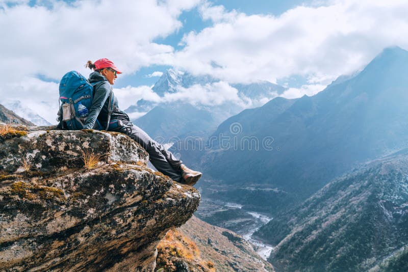 Young hiker backpacker female sitting on cliff edge and enjoying the Imja Khola valley during high altitude Everest Base Camp EBC trekking route near Phortse, Nepal. Active vacations concept image