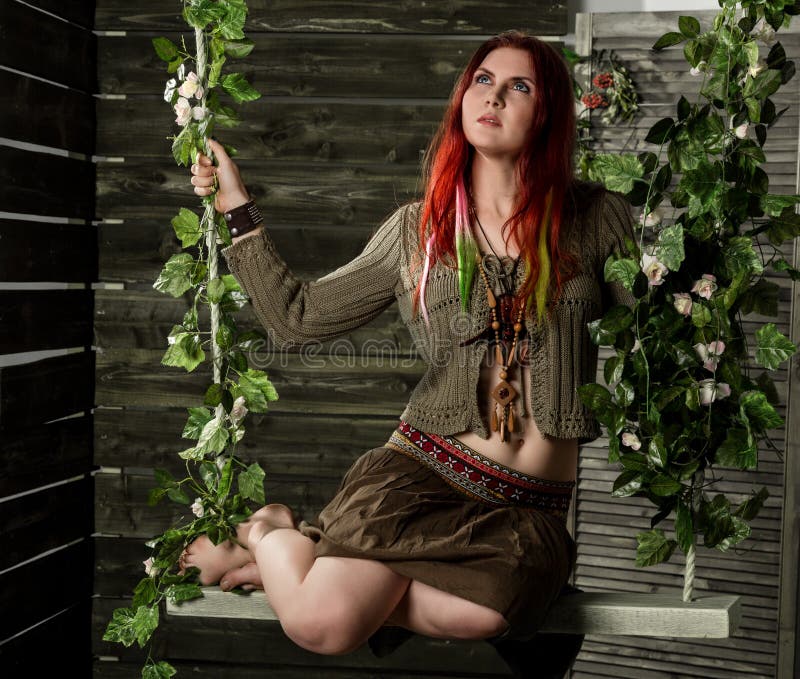 Young hippie boho redhead woman having fun on a swing. Hippie style on a wooden background