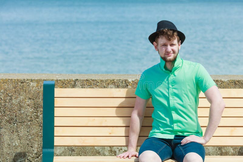 Young hipster man sitting on bench near the sea outdoor