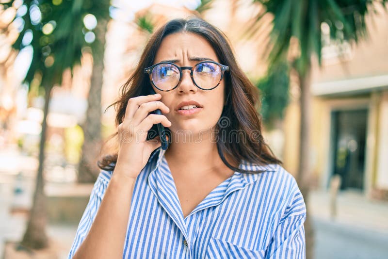 Young hispanic businesswoman with worried expression talking on the smartphone at the city