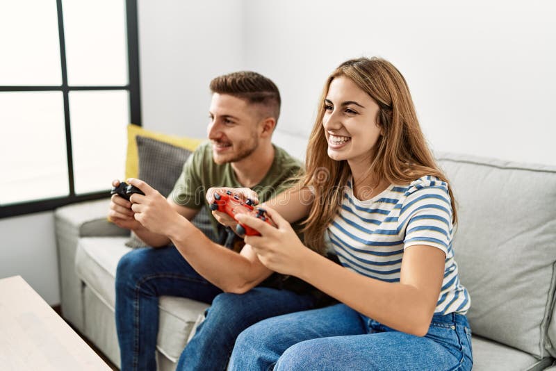 Young hispanic couple smiling happy playing video game sitting on the sofa with dog at home