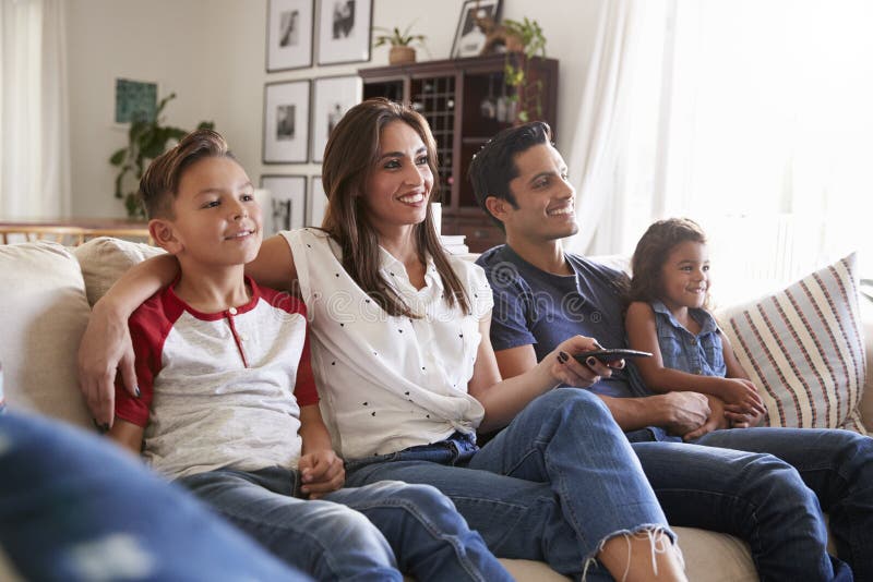 Young Hispanic family sitting on the sofa at home watching TV togther, close up