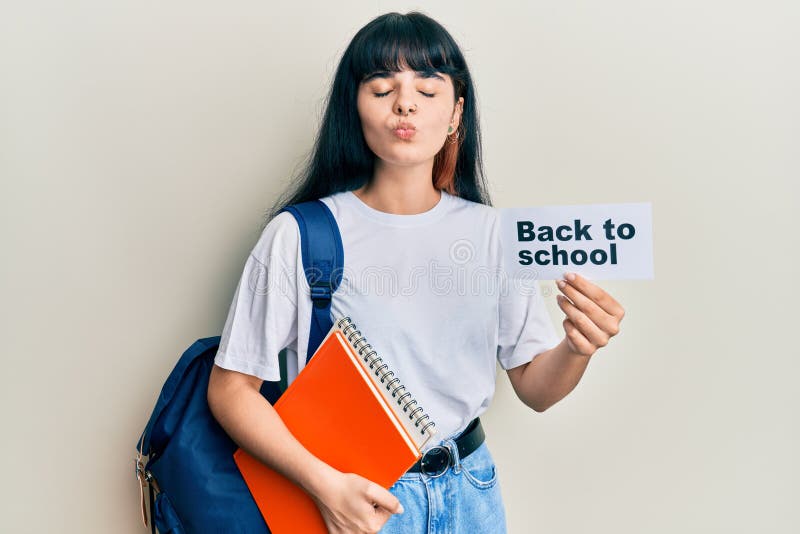 Young hispanic girl wearing backpack holding back to school banner looking at the camera blowing a kiss being lovely and sexy. love expression