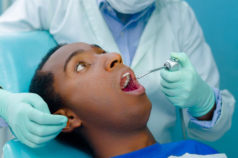 Young hispanic male lying in dental chair looking up, dentists hands with gloves holding tool into patients mouth stock photos Young hispanic male lying in dental chair looking up, dentists hands with gloves holding tool into patients mouth stock photos