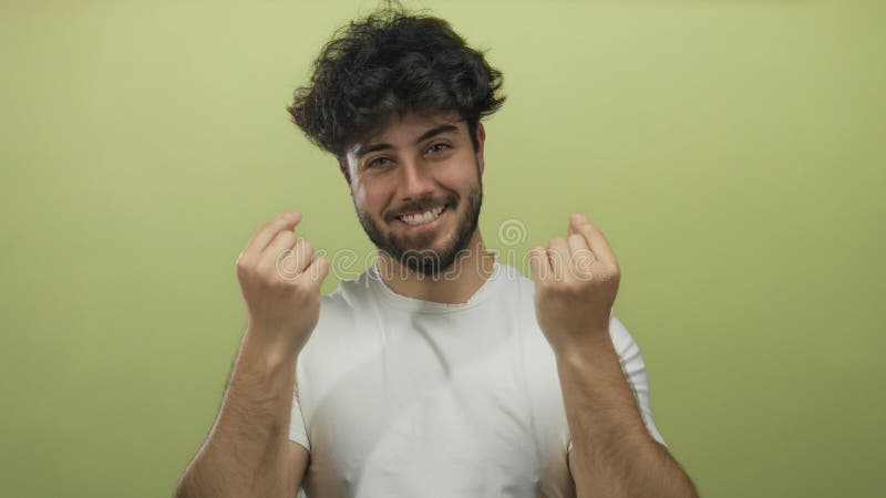 Young hispanic man with beard makes a heart gesture with his fingers against a vibrant yellow backdrop, expressing joy and stock image