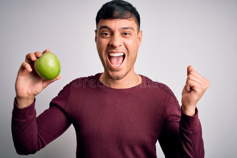 Young Hispanic Man Eating Fresh Green Apple As Healthy Nutrition Over ...