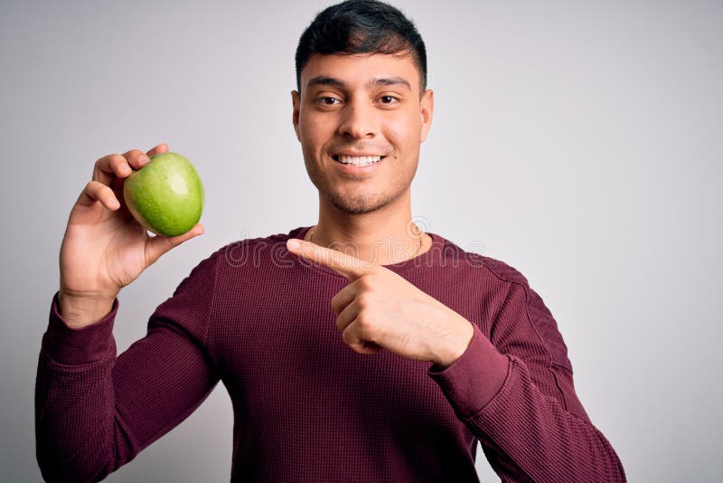 Young Hispanic Man Eating Fresh Green Apple As Healthy Nutrition Over ...