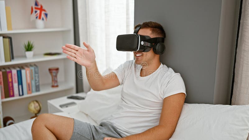 A young hispanic man experiences virtual reality wearing a headset in a cozy bedroom setting stock images