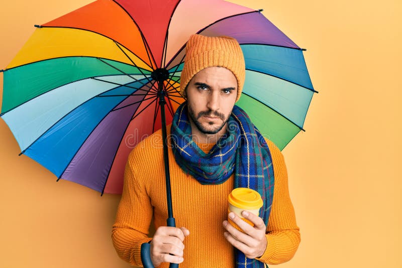 Young hispanic man holding colorful umbrella drinking take away coffee skeptic and nervous, frowning upset because of problem. negative person