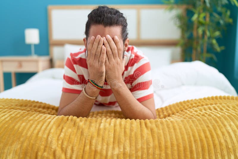 Young Hispanic Man Lying on Bed Covering Eyes with Hands at Bedroom