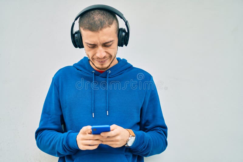 Young hispanic man with serious expression using smartphone and headphones at the city royalty free stock photo