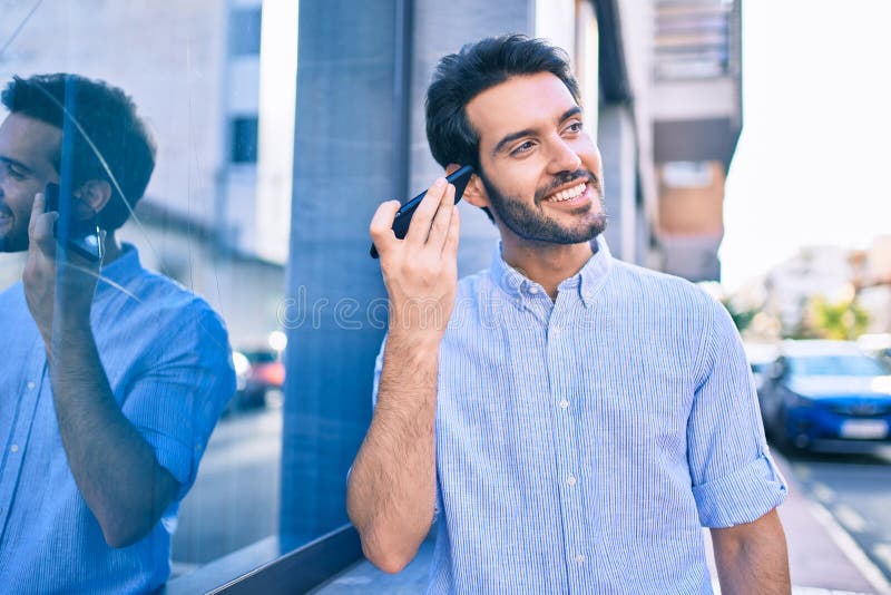Young hispanic man smiling happy listening audio message using smartphone at city stock photos
