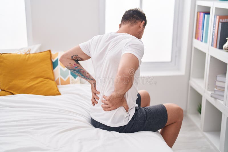 Young Hispanic Man Suffering for Back Injury Sitting on Bed at Bedroom