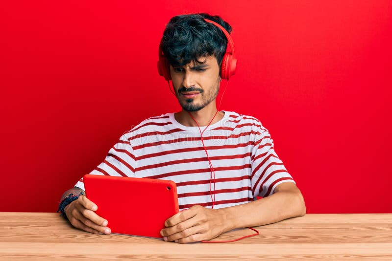 Young hispanic man using touchpad wearing headphones clueless and confused expression royalty free stock photos