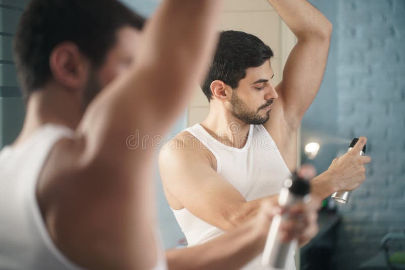 Young hispanic people and male beauty. Confident metrosexual man using spray deodorant on underarm skin, smiling and looking at mirror. Young hispanic people and male beauty. Confident metrosexual man using spray deodorant on underarm skin, smiling and looking at mirror.