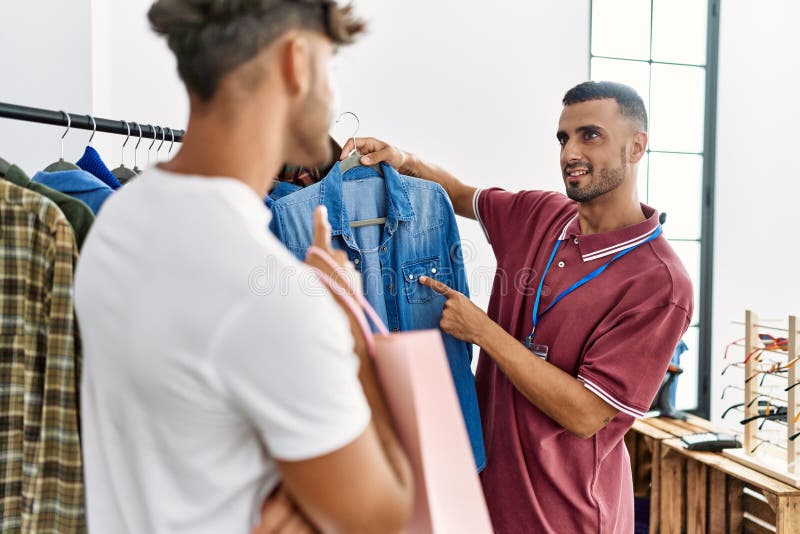 Young Hispanic Shopkeeper Showing Clothes To Customer at Clothing Store ...