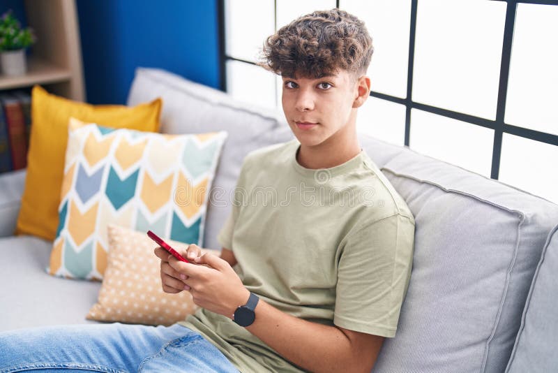 Young hispanic teenager using smartphone sitting on sofa at home stock images