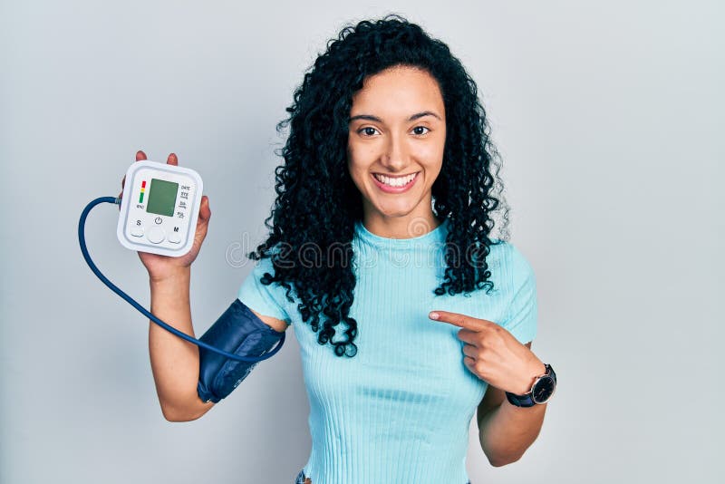 Young Hispanic Woman With Curly Hair Using Blood Pressure Monitor