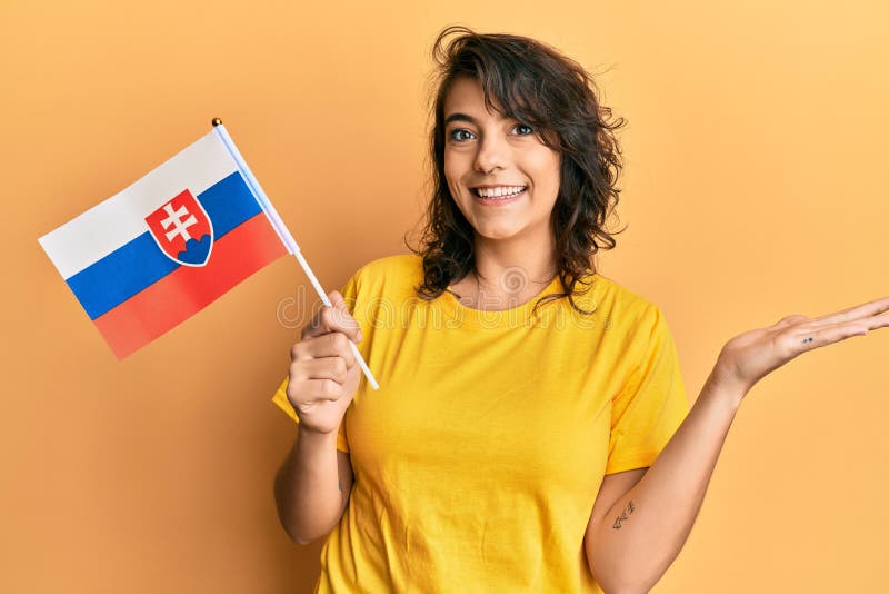 Mladá hispánka držiaca slovenskú vlajku oslavujúca úspech so šťastným úsmevom a víťazným výrazom so zdvihnutou rukou