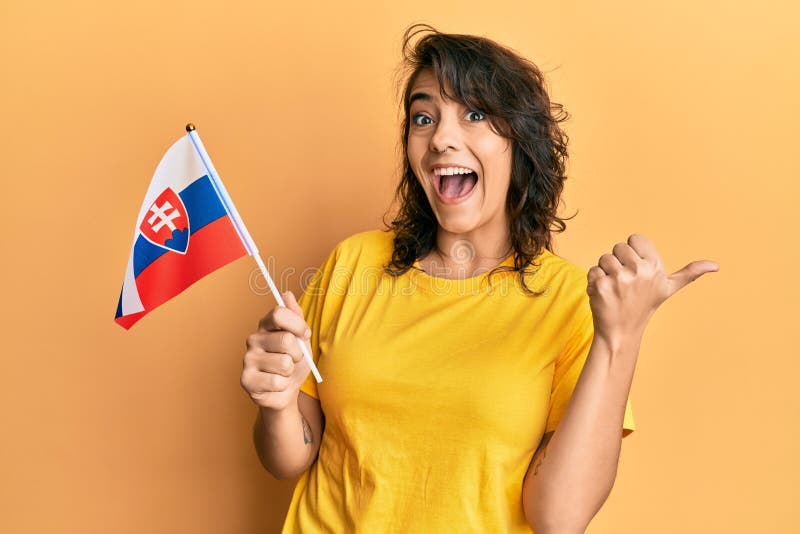Mladá hispánka drží slovenskú vlajku ukazujúcu palcom nahor s úsmevom šťastná s otvorenými ústami