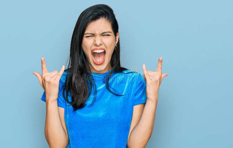 Young hispanic woman wearing casual clothes shouting with crazy expression doing rock symbol with hands up