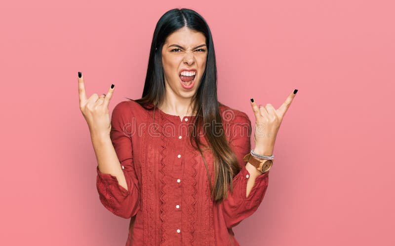 Young hispanic woman wearing casual clothes shouting with crazy expression doing rock symbol with hands up