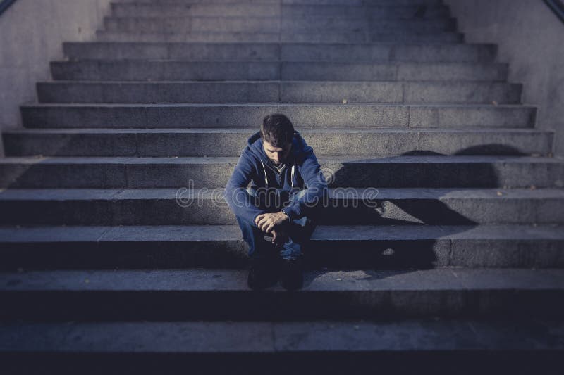 Young homeless man lost in depression sitting on ground street concrete stairs