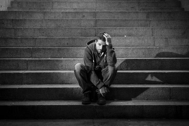 Young homeless man lost in depression sitting on ground street concrete stairs