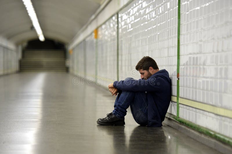 Young homeless man lost in depression sitting on ground street subway tunnel