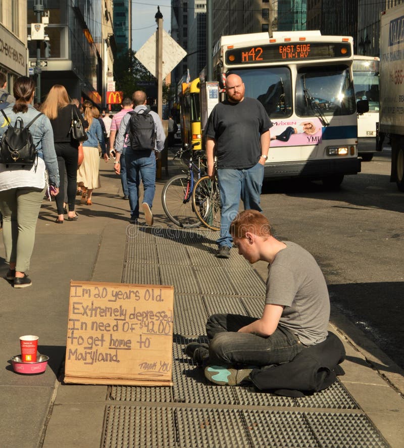 Young homeless man sitting and begging for money on city street.