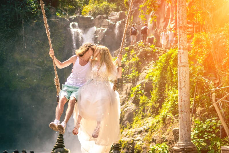 Young honeymoon couple swings in the jungle near the lake, Bali island, Indonesia.