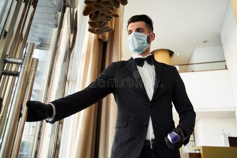 Elegant man in suit pulling the glass door handle and holding a contactless thermometer. Elegant man in suit pulling the glass door handle and holding a contactless thermometer