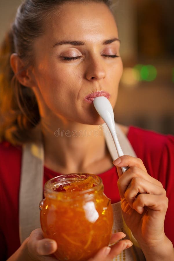 Young housewife tasting a spoon of homemade orange marmalade