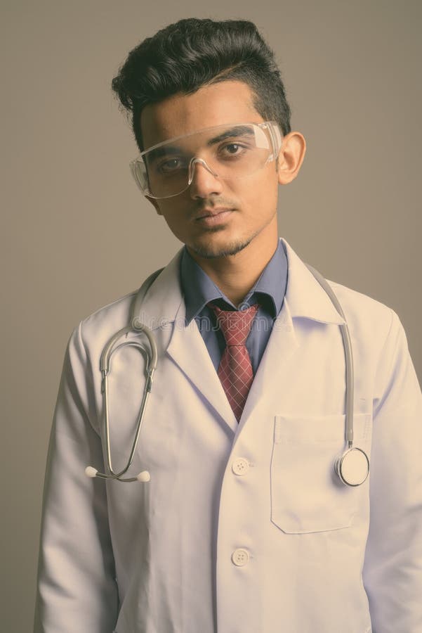 Young Indian man doctor wearing protective glasses against gray background stock photo Young Indian man doctor wearing protective glasses against gray background stock photo