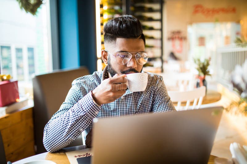 Young Indian Man Drinking Coffee in Cafe and Using Laptop in Cafe Stock