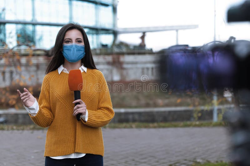 Journalist with medical mask and microphone working on city street. Virus protection