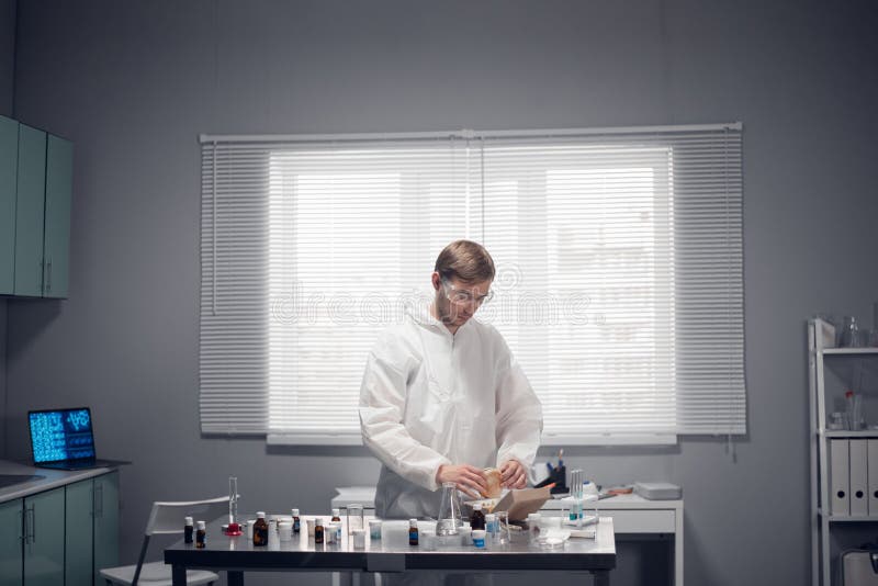 A young lab worker having a lunch break, eating a burger in his office stock photography