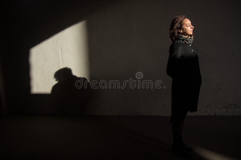 The young lady in black stylish coat with black scarf enjoying the sun rays at sunset in the white tunnel in the cold autumn day and black shadow on the white wall. The young lady in black stylish coat with black scarf enjoying the sun rays at sunset in the white tunnel in the cold autumn day and black shadow on the white wall