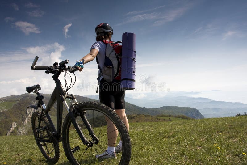 Female cyclist holding her bike and admiring the view of the mountains. Female cyclist holding her bike and admiring the view of the mountains