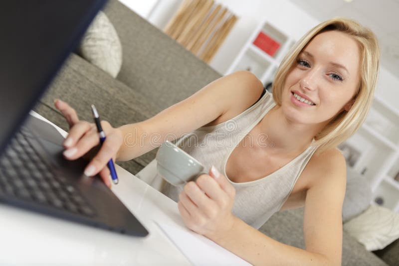 Young lady at home drinking coffee while using laptop