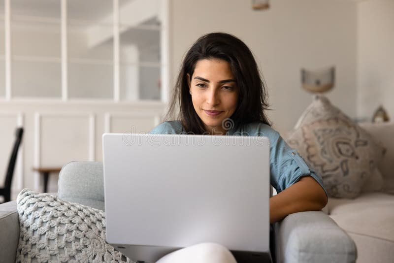 Young Latina woman sitting comfortable on sofa with modern laptop royalty free stock photography