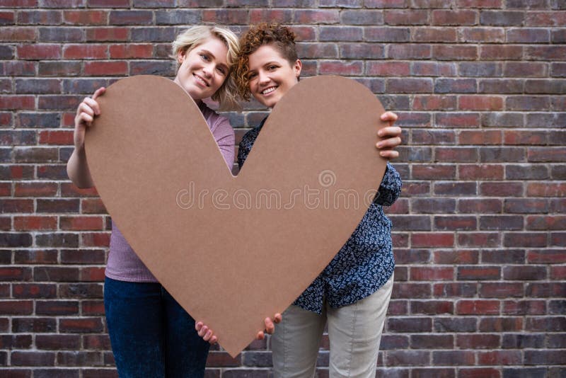 Young lesbian couple smiling contently while holding a heart outside royalty free stock photo Young lesbian couple smiling contently while holding a heart outside royalty free stock photo
