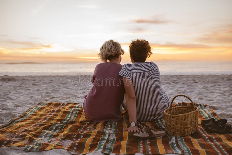 Young Lesbian Couple Watching A Romantic Sunset At The Beach Stock