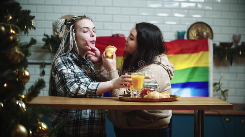 Two Lesbian Women Kissing And Eating Croissants While Having Breakfast