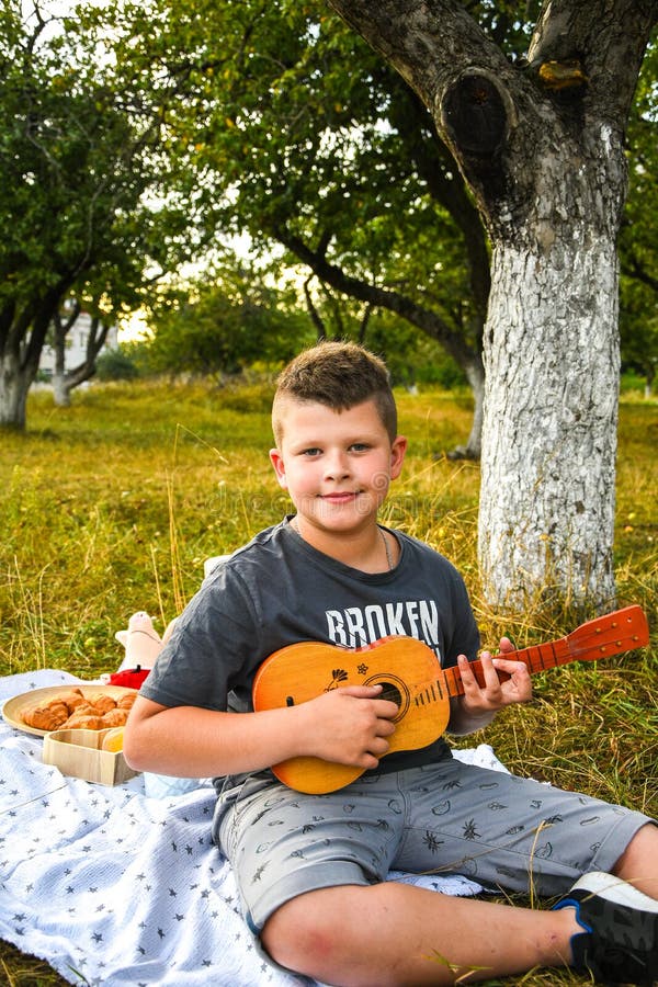 Young little boy guitarist outdoor. Boy on city park summer meadow enjoying day playing guitar