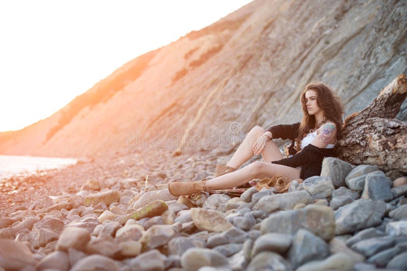 Sad lonely Brunette brunette girl in a Boch chic style sitting on gray stones stock image Sad lonely Brunette brunette girl in a Boch chic style sitting on gray stones stock image