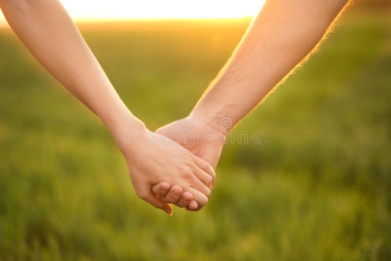 Young lovely couple holding hands in green field