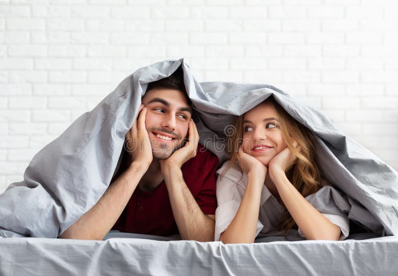 Young loving couple lying in bed under blanket stock photos Young loving couple lying in bed under blanket stock photos