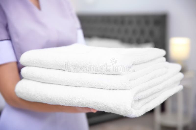 Young maid holding stack of towels in hotel room royalty free stock image